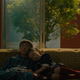 A young Chinese girl cuddles up to an unresponsive android on an orange couch.